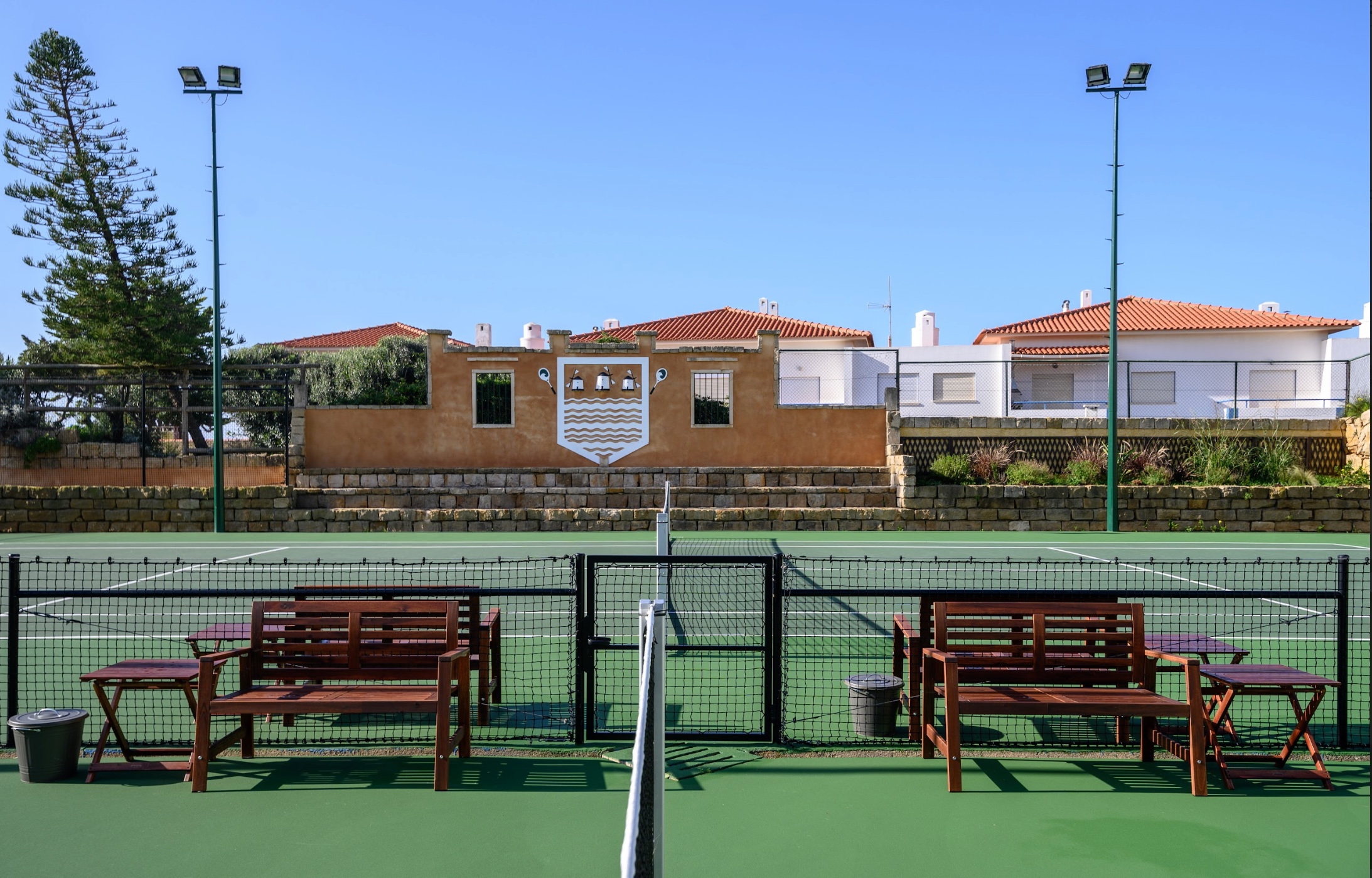 Green hard court with wooden benches and Portuguese village backdrop in Ericeira